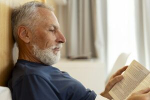 Closeup, handsome, serious senior man reading book, lying in bed, morning routine