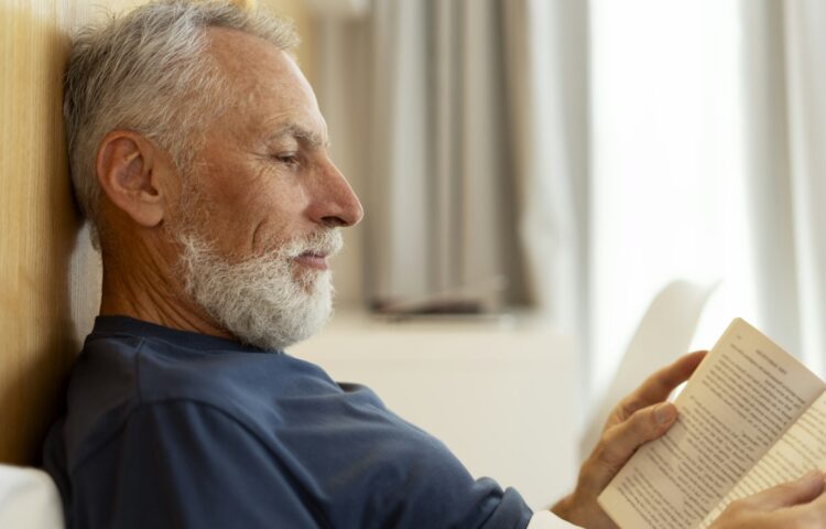 Closeup, handsome, serious senior man reading book, lying in bed, morning routine