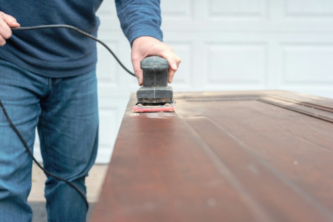 Man using an electric sander to refinish doors