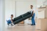 Holding heavy sofa. Two moving service employees in a room