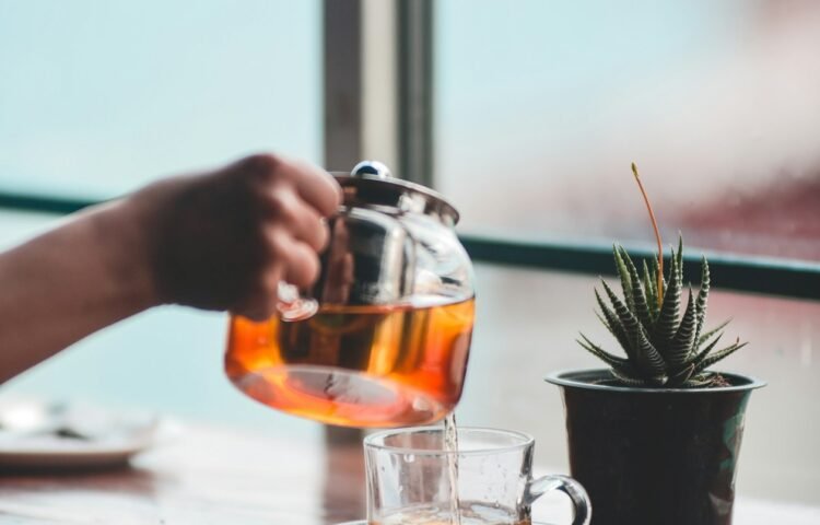Pouring tea into a glass cup by a window